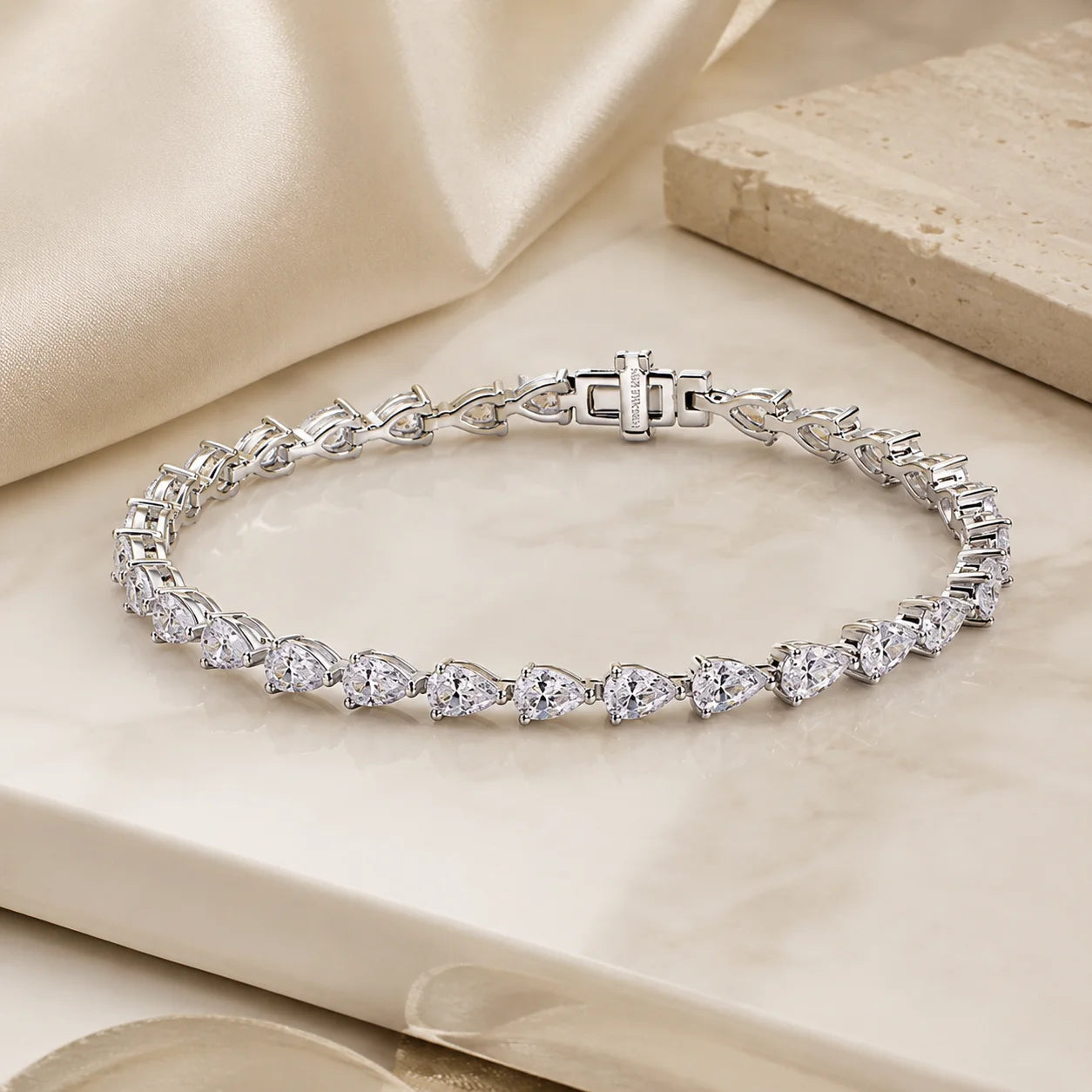Full view of the Langley™ pear-cut moissanite tennis bracelet for women arranged in a complete circle on a beige luxury surface.