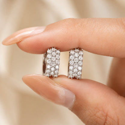 Moissanite hoop earrings held between fingers, showing brilliant stones and compact luxury design.