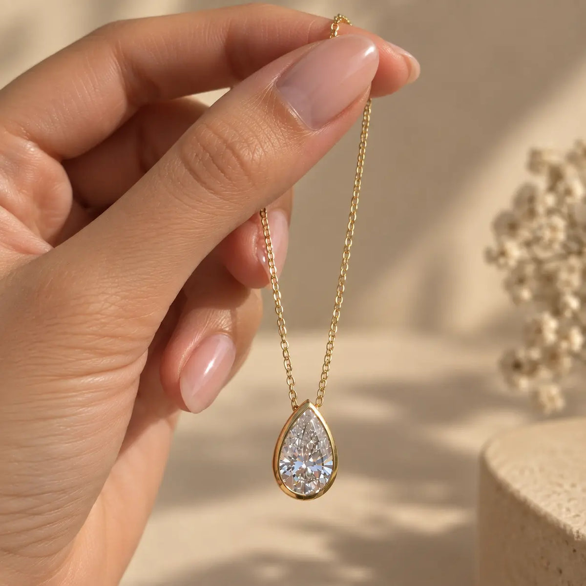 Hand holding a delicate pear cut moissanite pendant necklace in a gold tone finish