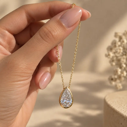 Hand holding a delicate pear cut moissanite pendant necklace in a gold tone finish
