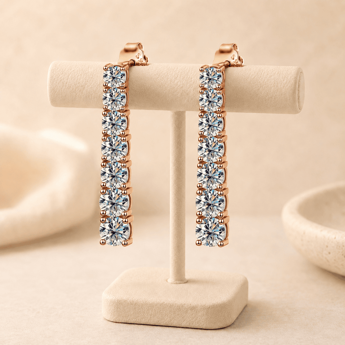 Rose gold moissanite drop earrings displayed on a beige jewelry stand with brilliant stones and soft luxury background.