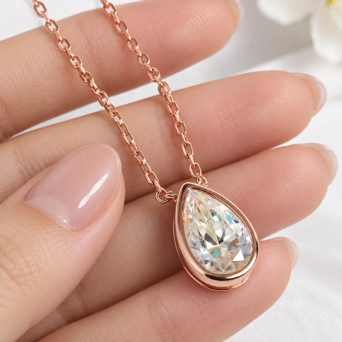 Rose gold tone pear cut moissanite pendant necklace shown in a detailed hand-held view