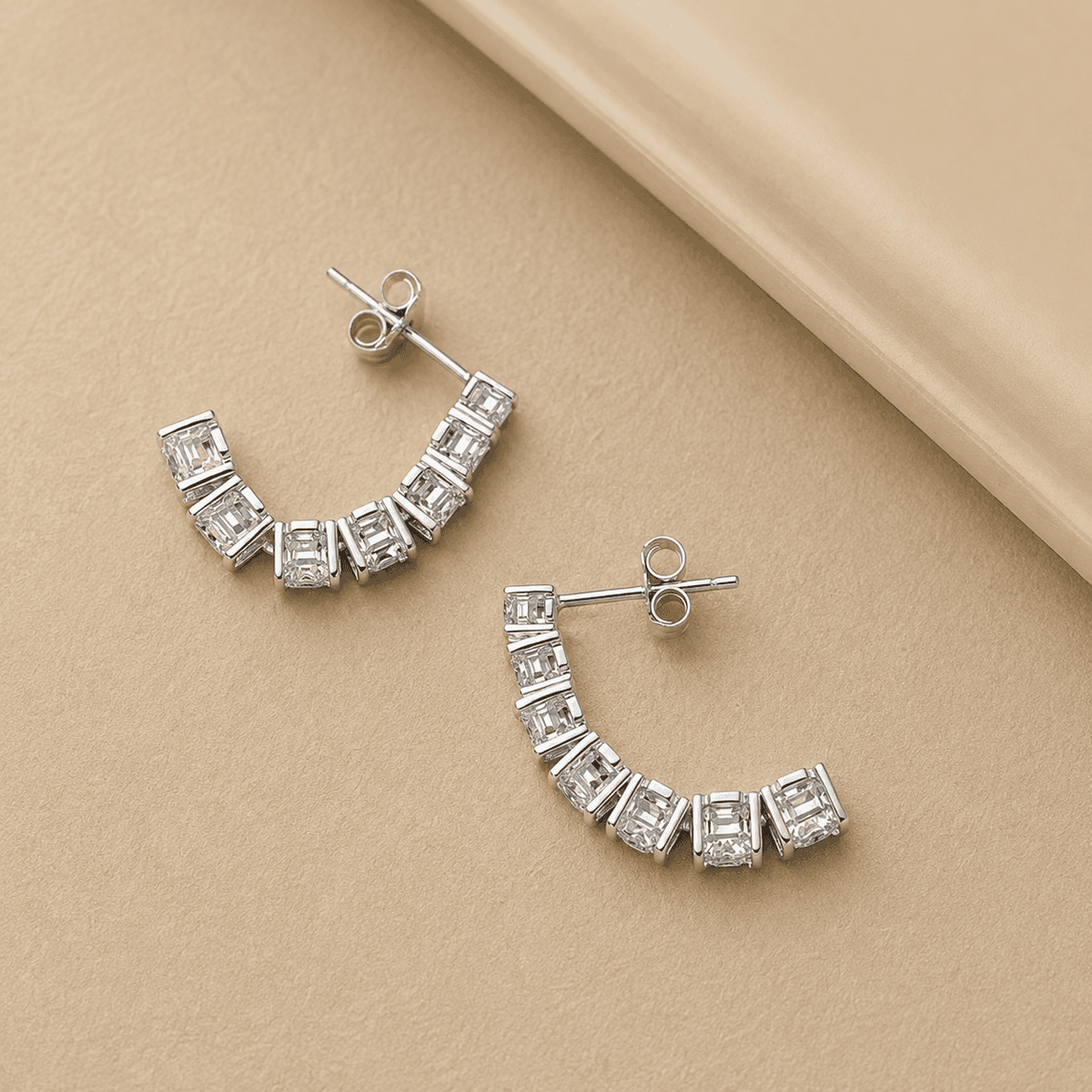 Silver moissanite drop earrings displayed on a beige jewelry stand with brilliant stones and luxury presentation.