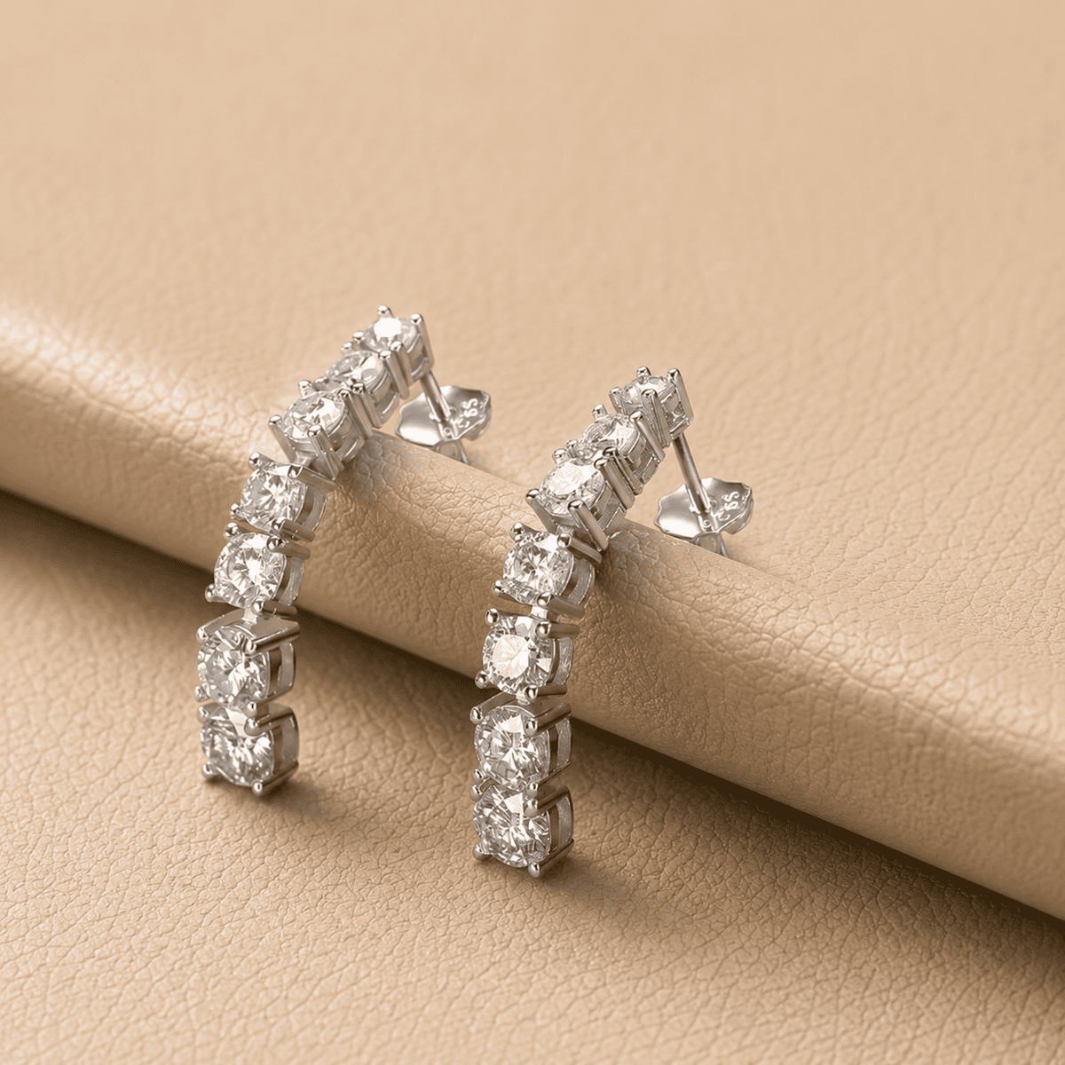 Silver curved moissanite earrings resting on beige leather with sparkling stones and elegant product styling.