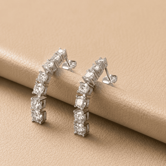 Silver curved moissanite earrings resting on beige leather with sparkling stones and elegant product styling.