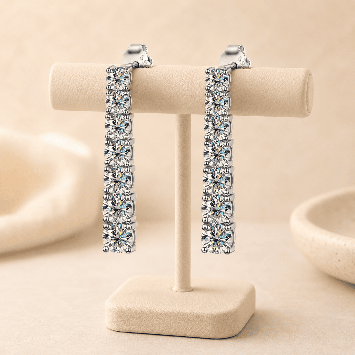 Silver moissanite drop earrings displayed on a beige jewelry stand with brilliant stones and luxury presentation.