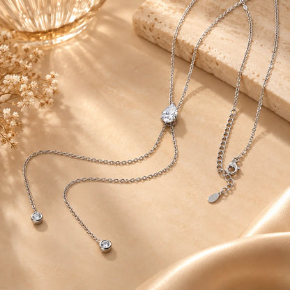 Silver tone moissanite lariat drop necklace arranged on a warm beige satin surface