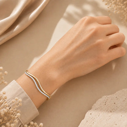 Woman wearing a wave moissanite bangle bracelet on the wrist in an elegant beige luxury setting.